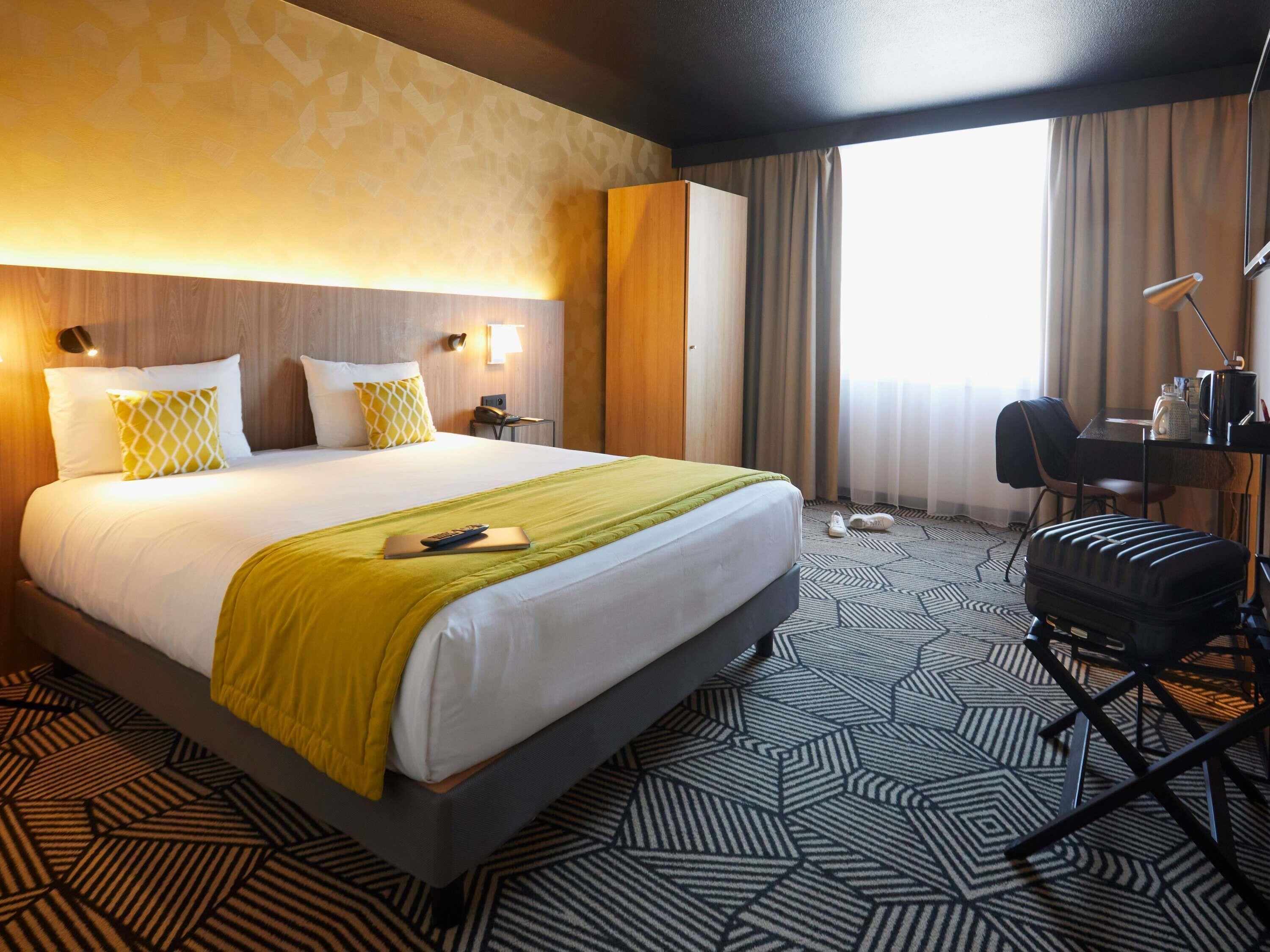 Ein Hotelzimmer mit einem großen Bett, einem Schreibtisch, einem Stuhl und Blick ins Freie.