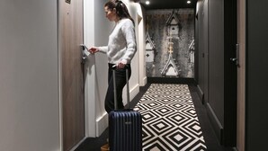 A hallway with a geometric patterned floor, a person with a suitcase, and a door with a number sign. - Mercure Arras Centre Gare (Arras)