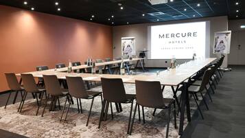 Un salón de conferencias con una larga mesa, sillas, una pantalla de proyector y una presentación titulada 'MERCURE HOTELS ARRAS CENTRE GARE'.