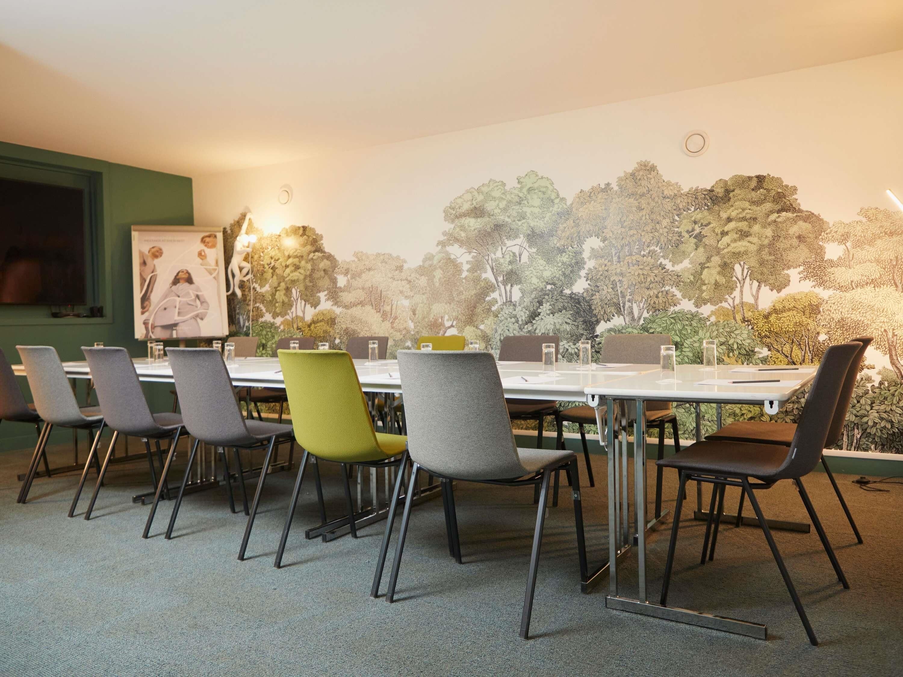 Une salle de conférence avec une longue table, de nombreuses chaises et une fresque représentant des arbres sur le mur.