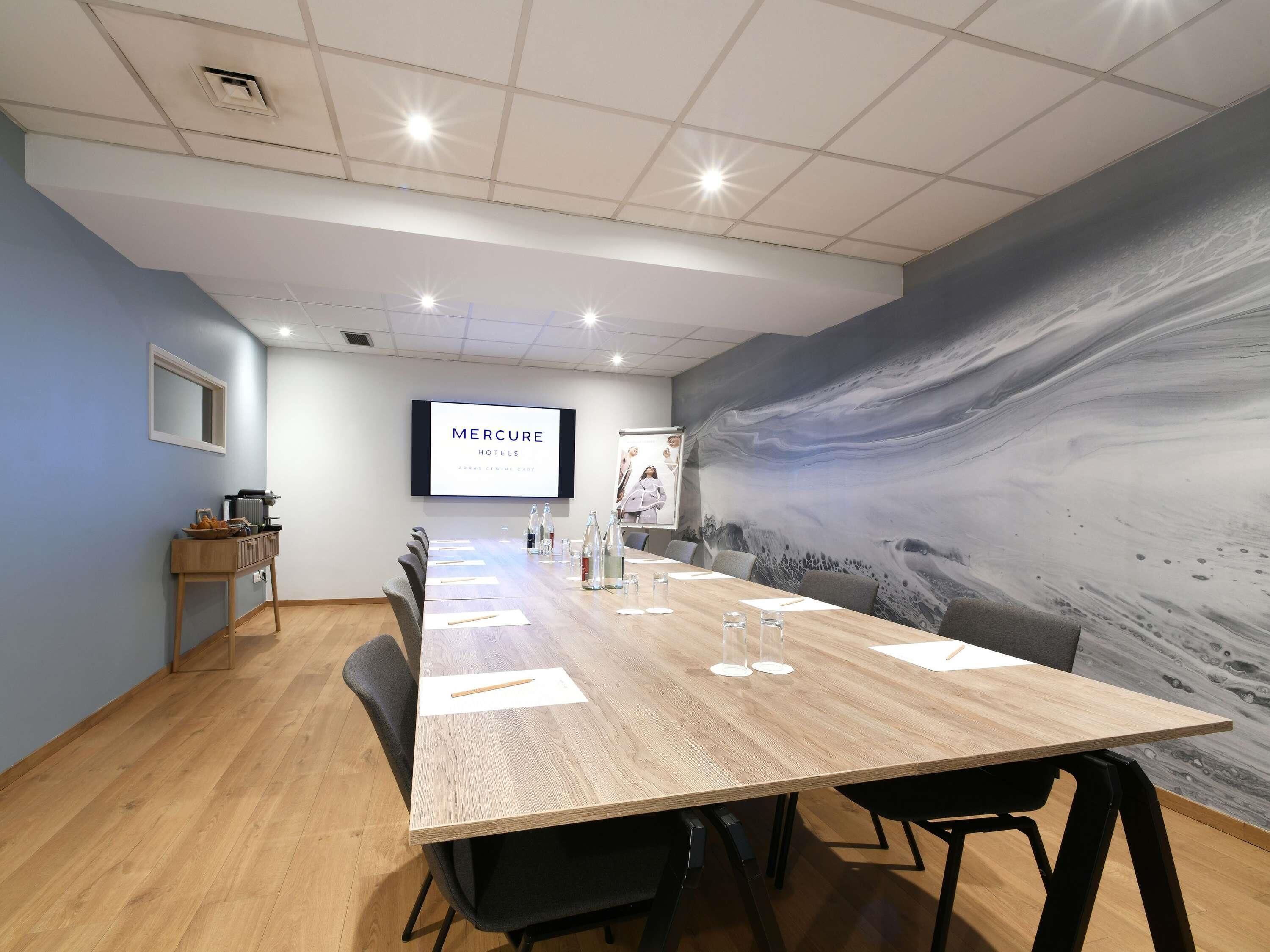 A conference room with a long table, chairs, a projector screen, and a large abstract mural on the wall.