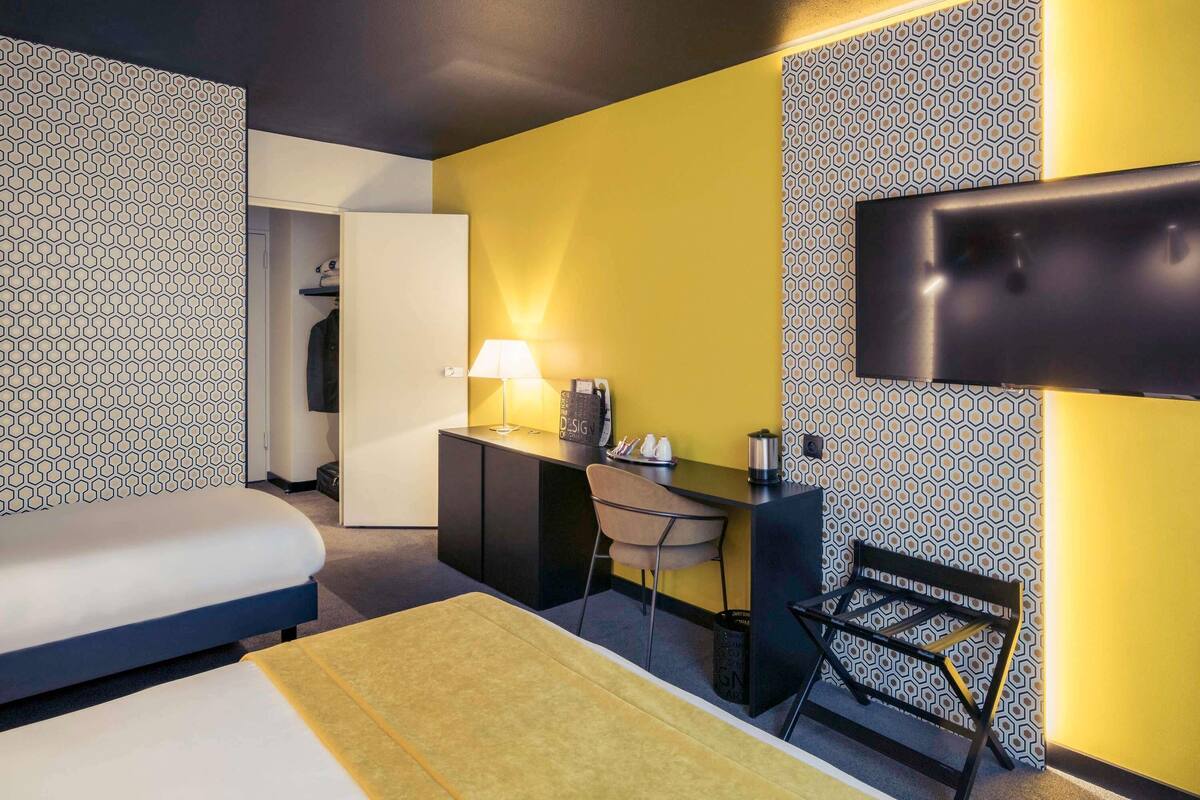 A hotel room with a bed, desk, chair, and a TV mounted on the wall.