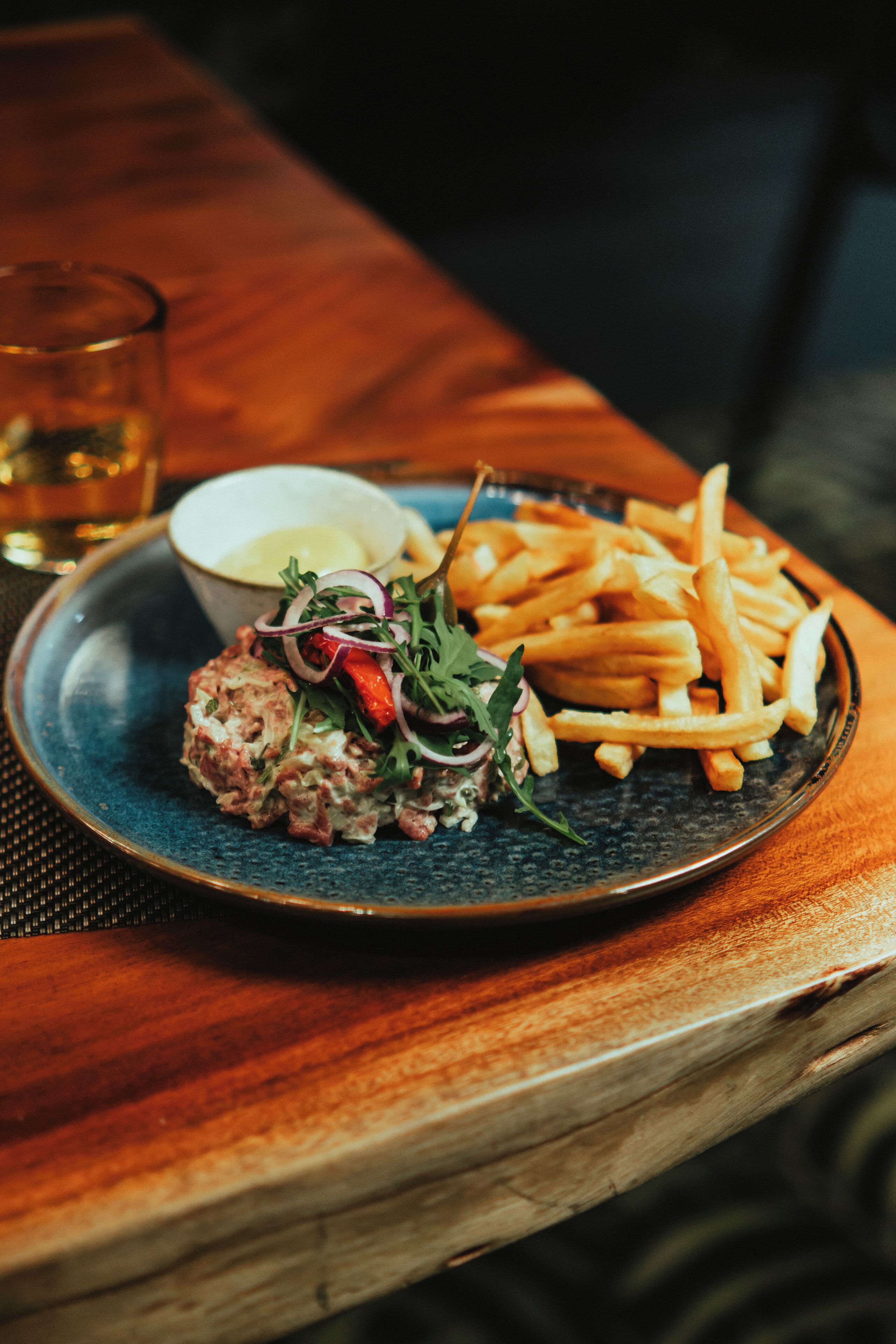A plate with food, a glass, and a bowl on a wooden table.