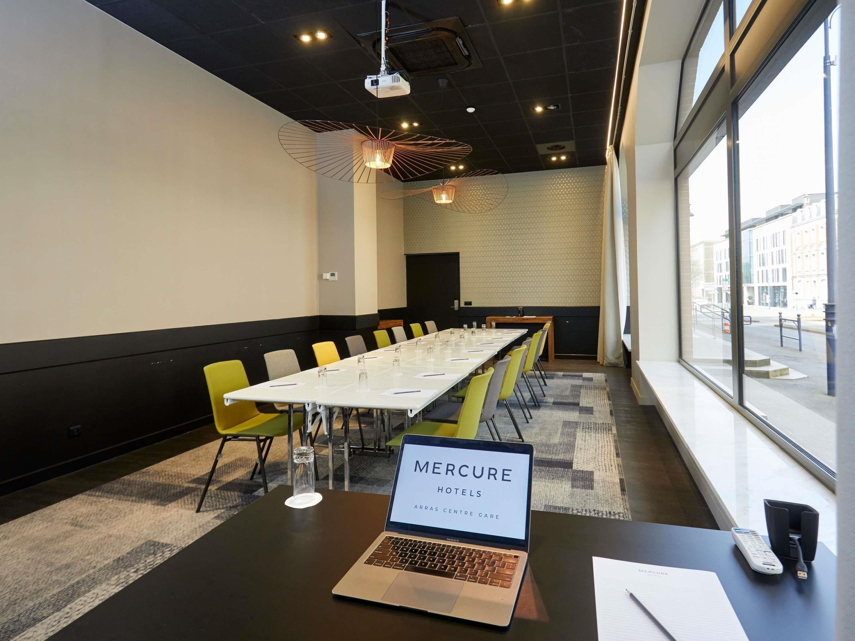 A conference room with a long table, chairs, a laptop, and a window with a city view.