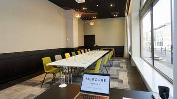 A conference room with a long table, chairs, a laptop, and a window with a city view.