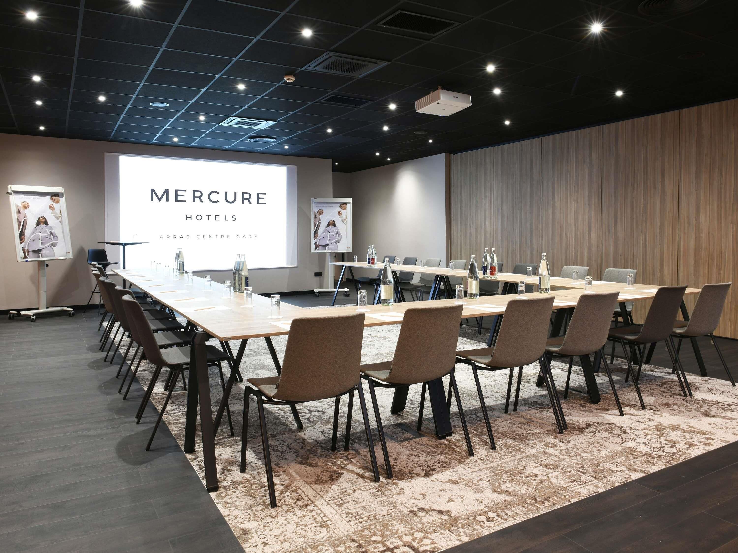 A conference room with a long table, chairs, a projector screen, and a wooden accent wall.