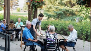 Un patio al aire libre con mesas y sillas, rodeado de follaje y una cerca.