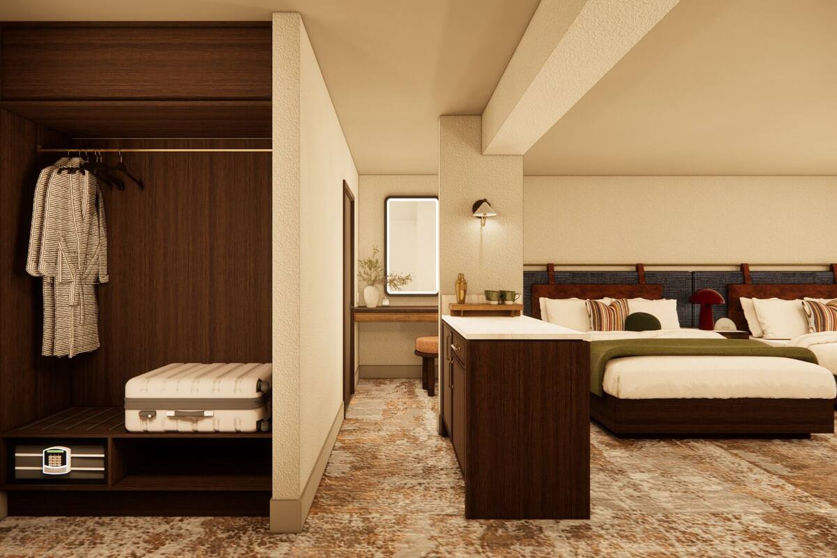 A hotel room with a walk-in closet, a bed with multiple pillows, a bedside table, and a mirror.