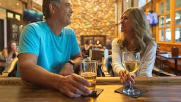 Un homme et une femme sont assis à une table en bois dans un restaurant. On aperçoit, en arrière-plan, un mur de pierre et des poutres en bois.