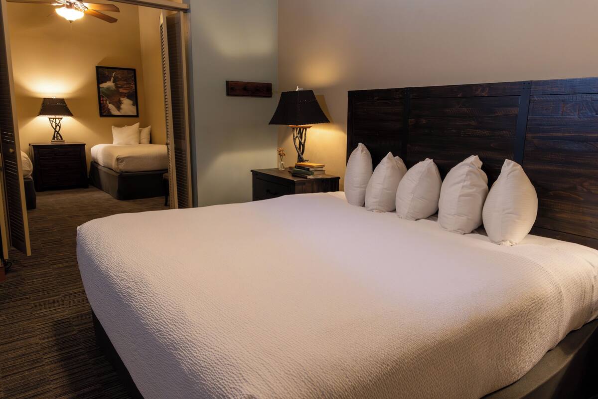 A neatly made bed with a headboard, two bedside tables with lamps, a framed picture on the wall, and a carpeted floor.