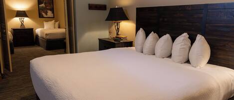 A neatly made bed with a headboard, two bedside tables with lamps, a framed picture on the wall, and a carpeted floor.