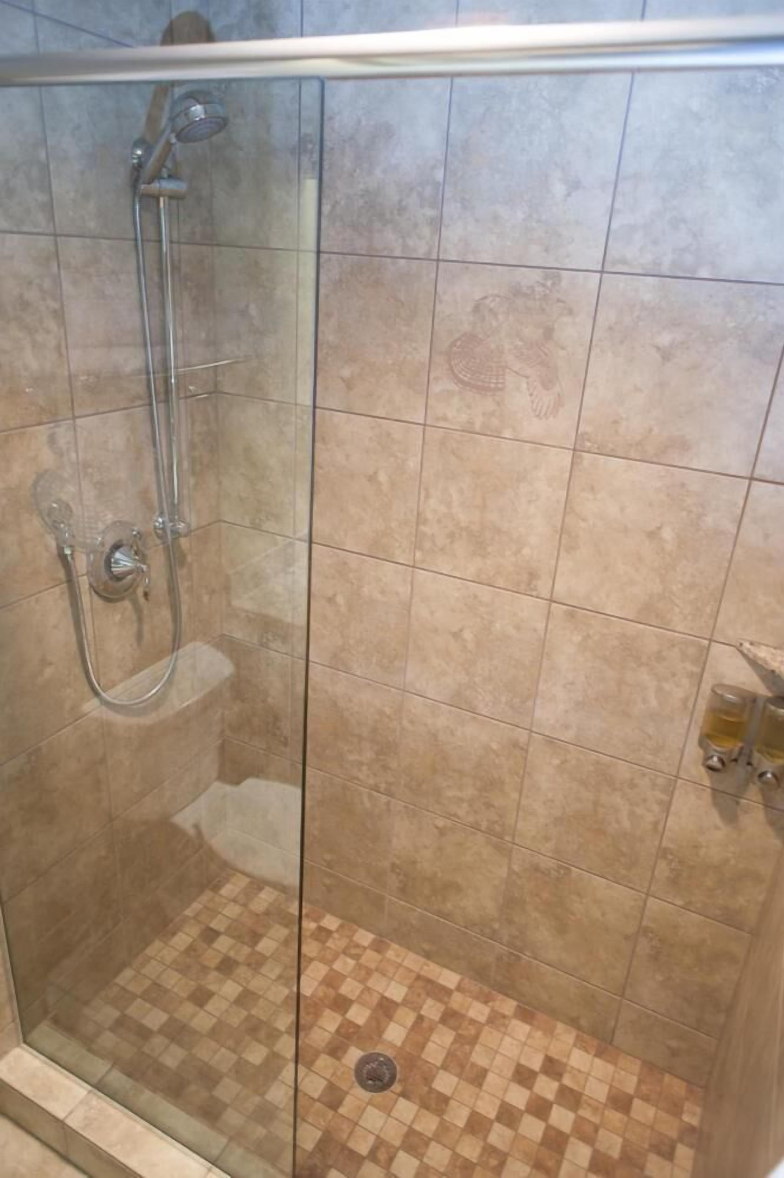 Ducha con mampara de vidrio, suelo de azulejos y cabezal de ducha.