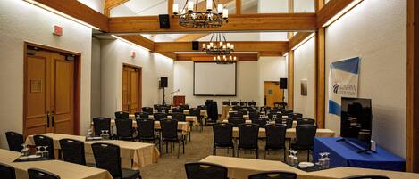 A conference room with multiple tables and chairs, wooden beams on the ceiling, and a projector screen.