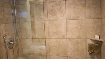 A shower with a glass door, a handheld showerhead, and a wall-mounted faucet.