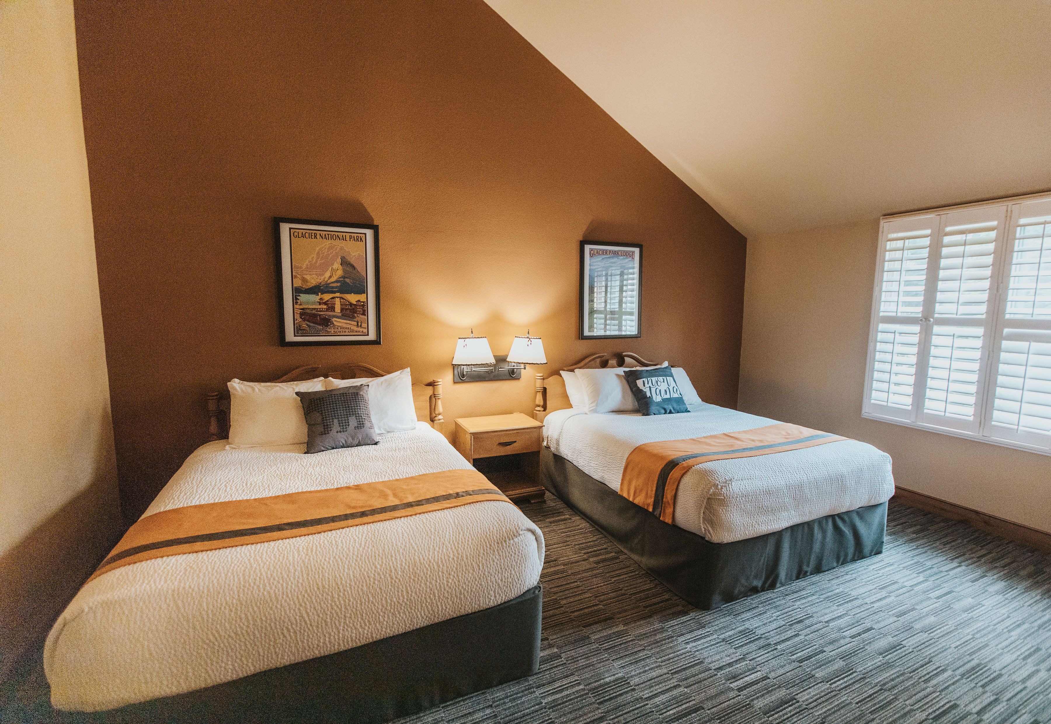 A hotel room with two beds, a nightstand, a lamp, and framed pictures on the wall.