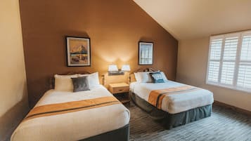 A hotel room with two beds, a nightstand, a lamp, and framed pictures on the wall.