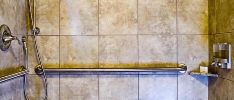 A shower area with a handrail, a wall-mounted faucet, and a tiled floor.