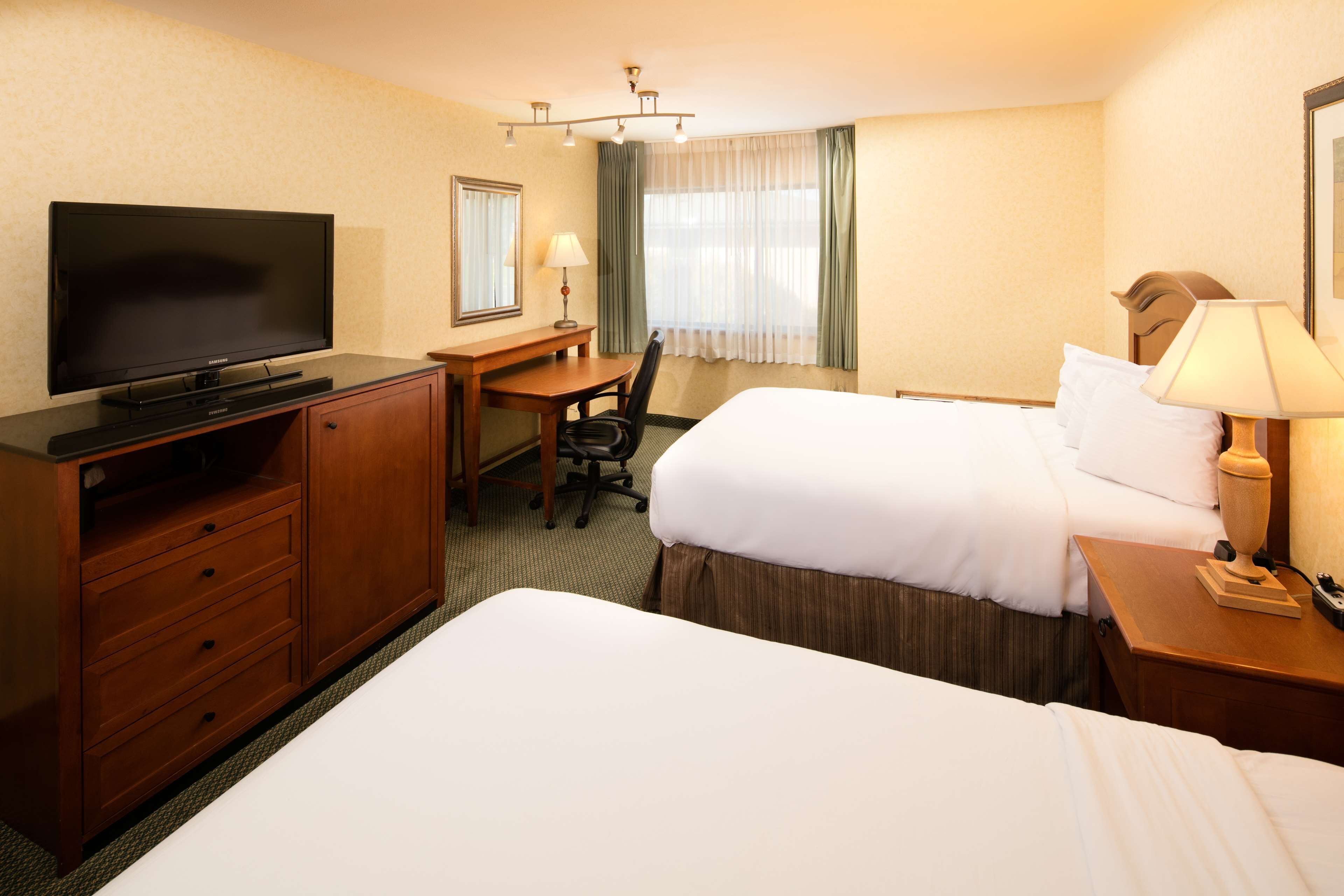 A hotel room with two beds, a desk with a chair, a television, and a lamp.