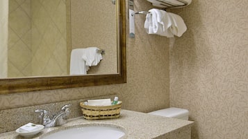 Un baño con lavamanos, espejo, toallero y papel tapiz estampado.