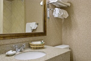 Un baño con lavamanos, espejo, toallero y papel tapiz estampado.