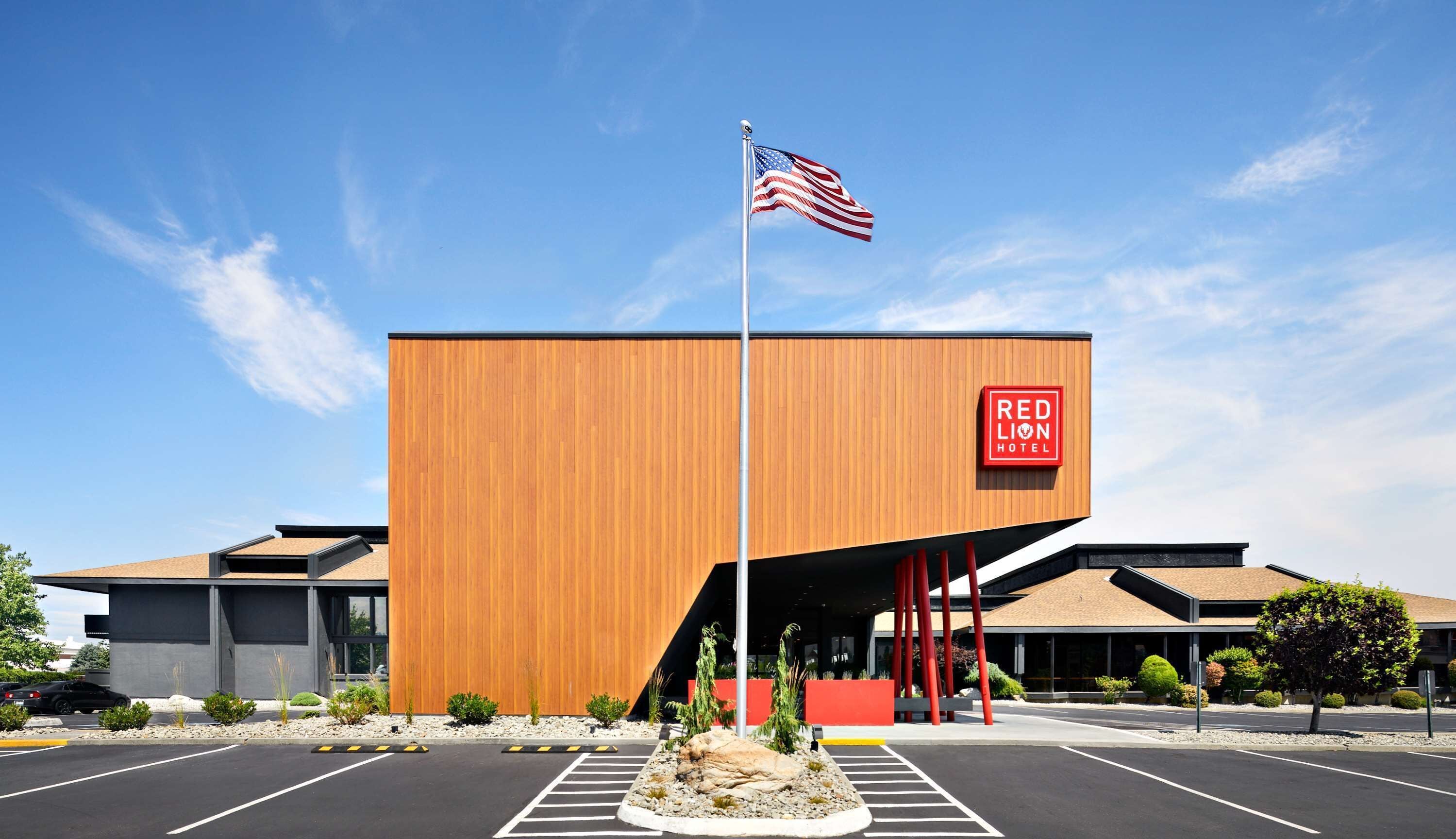 A modern hotel with a wooden facade, a flagpole with an American flag, and a sign reading "RED LION HOTEL".