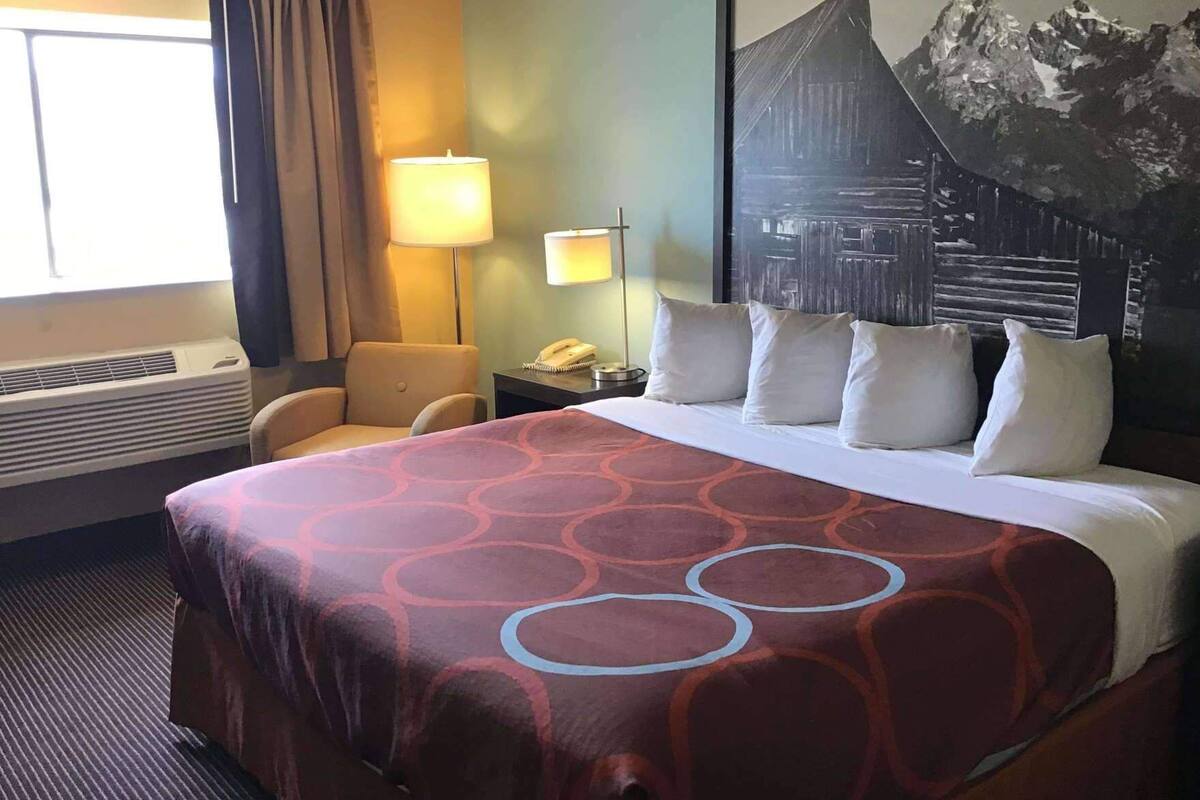 A hotel room with a large bed, a desk with a lamp, a chair, and a wall-mounted phone.