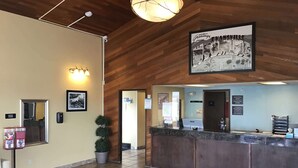 Un área de recepción con techo de madera, mostrador de recepción, letrero de bienvenida enmarco, teléfono y basurero.