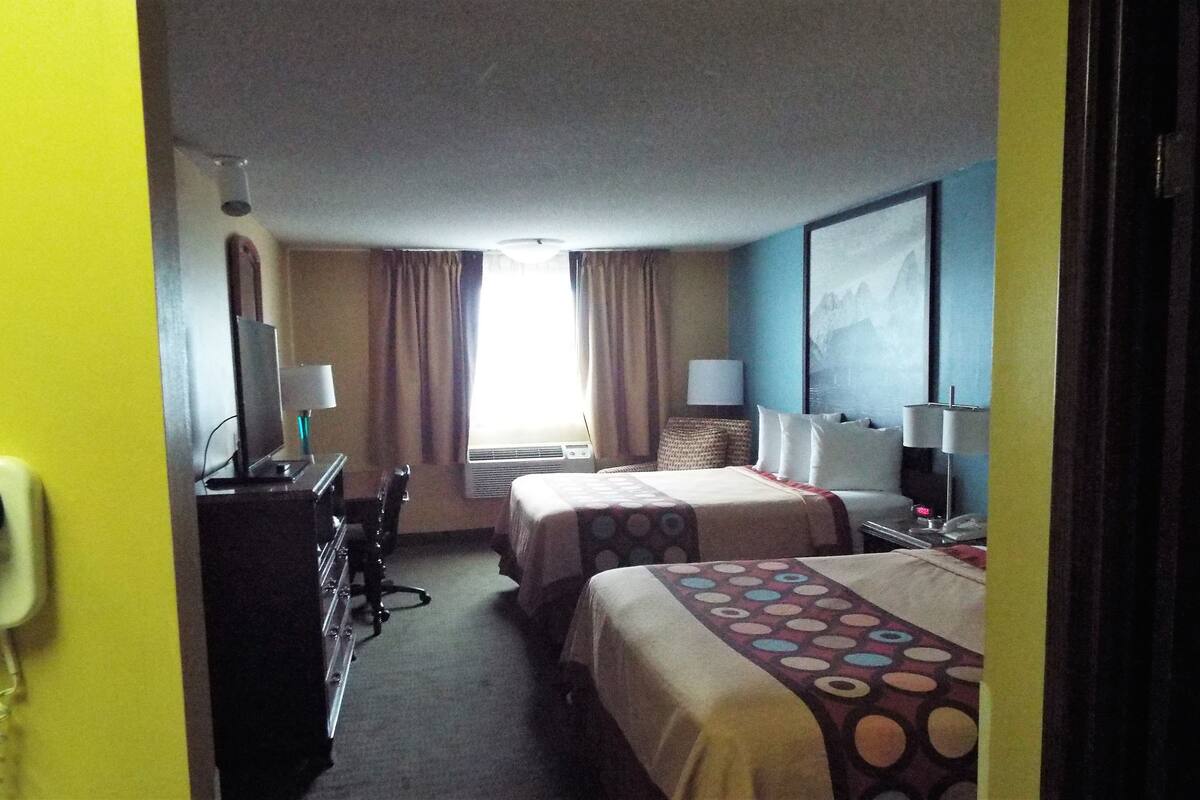 A hotel room with two beds, a desk, a lamp, a telephone, and a window with curtains.