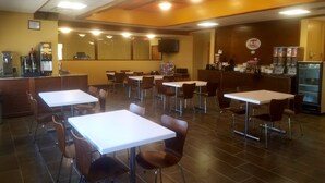 Un restaurante con varias mesas y sillas, una barra con caja registradora y un refrigerador.