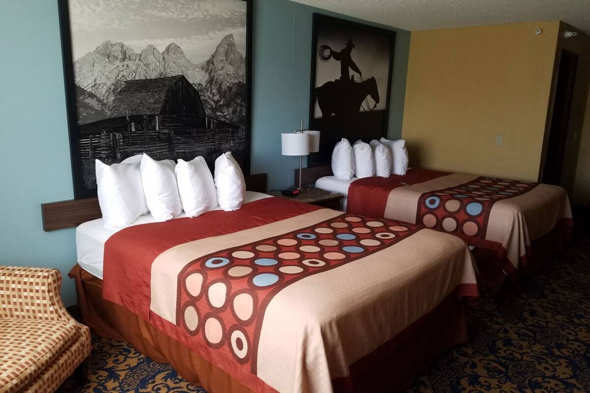 A hotel room with two beds, a large mountain painting, a cowboy silhouette, and a patterned carpet.