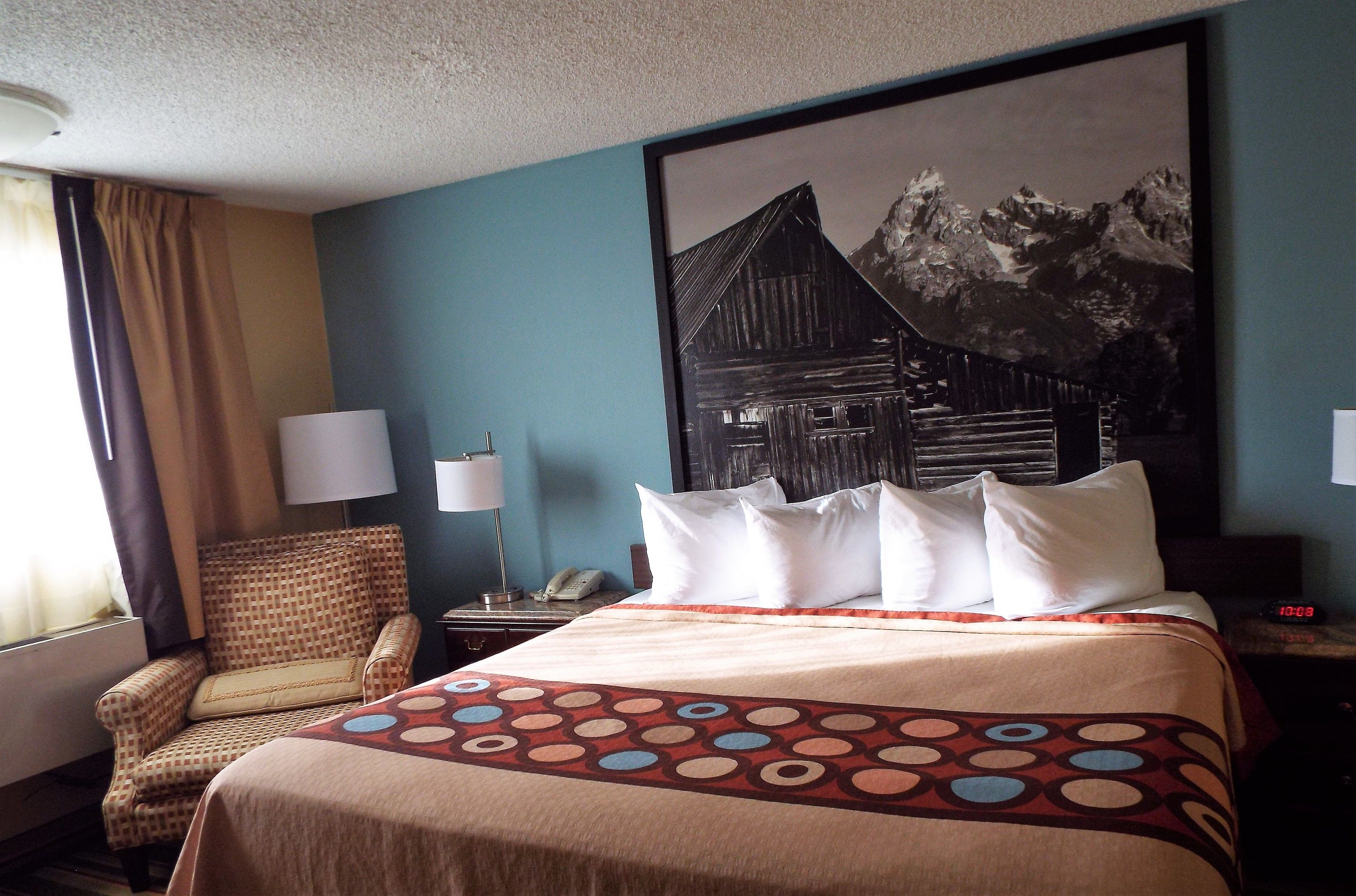 A hotel room with a bed, a chair, a nightstand, a lamp, and a painting on the wall.