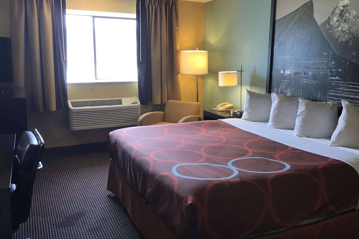 A hotel room with a large bed, a desk with a lamp, a chair, and a window with curtains.