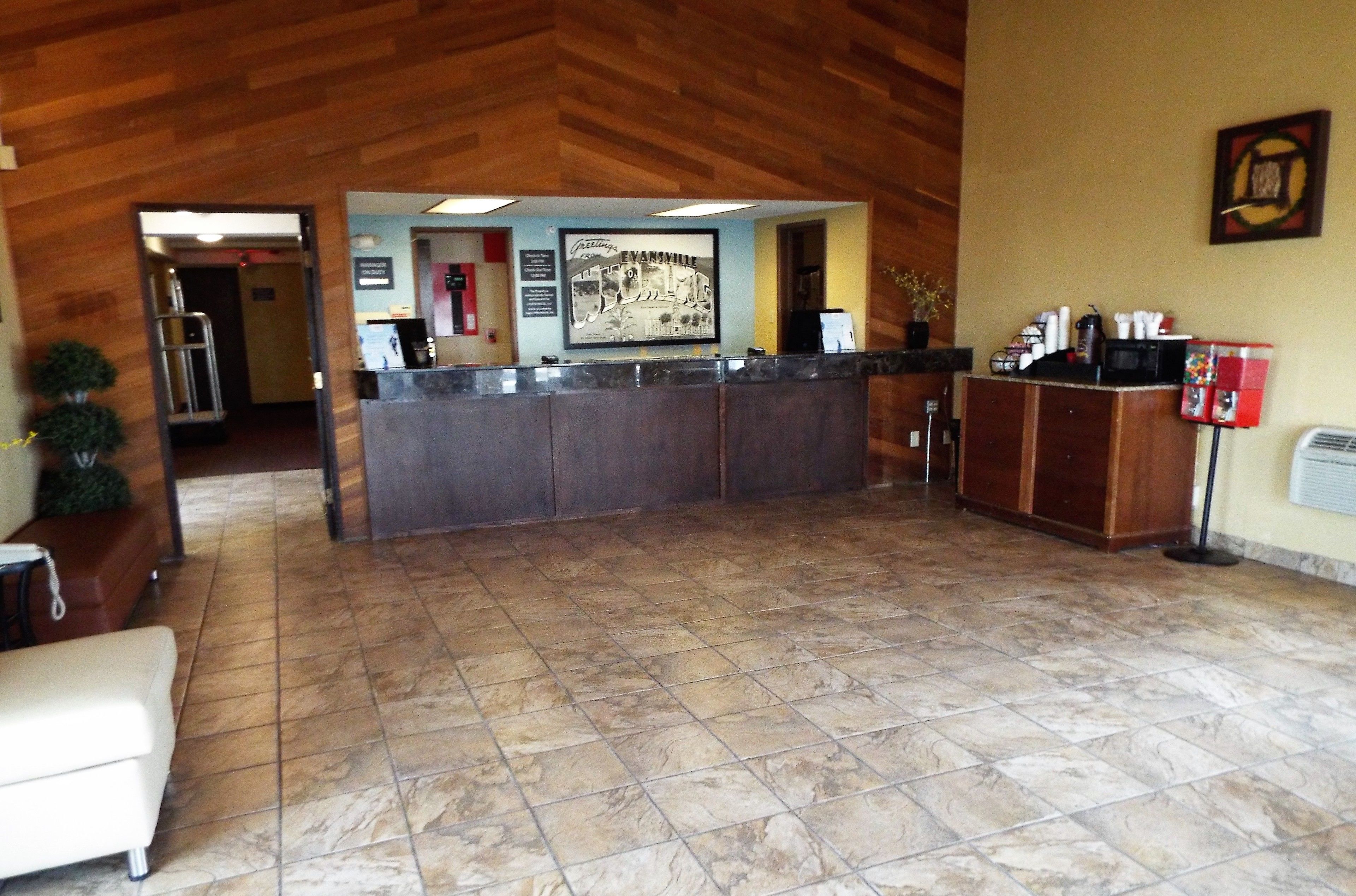 A reception area with a marble floor, wooden ceiling, and a reception desk. There is a framed picture on the wall and a small plant on the desk.