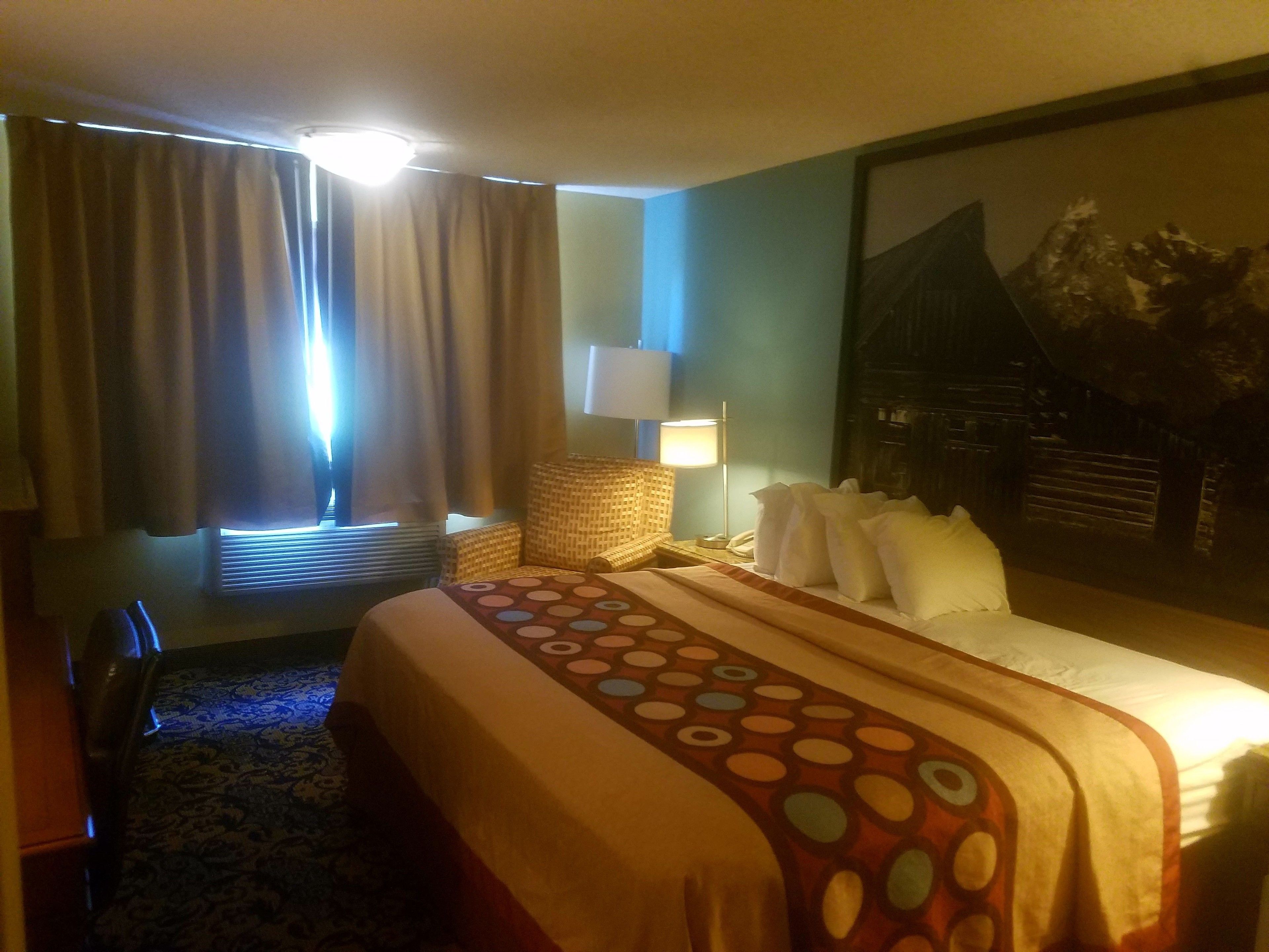 A hotel room with a bed, a chair, a lamp, and a large painting on the wall.