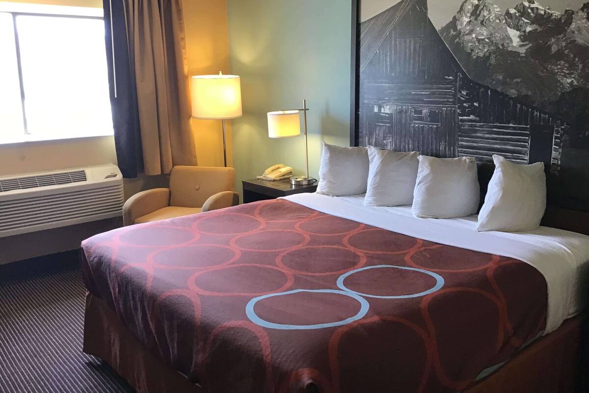 A hotel room with a large bed, a desk with a lamp, a chair, and a window with curtains.