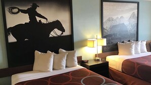 Una habitación de hotel con dos camas, una mesita de noche con lámpara y dos cuadros enmarcados en la pared.