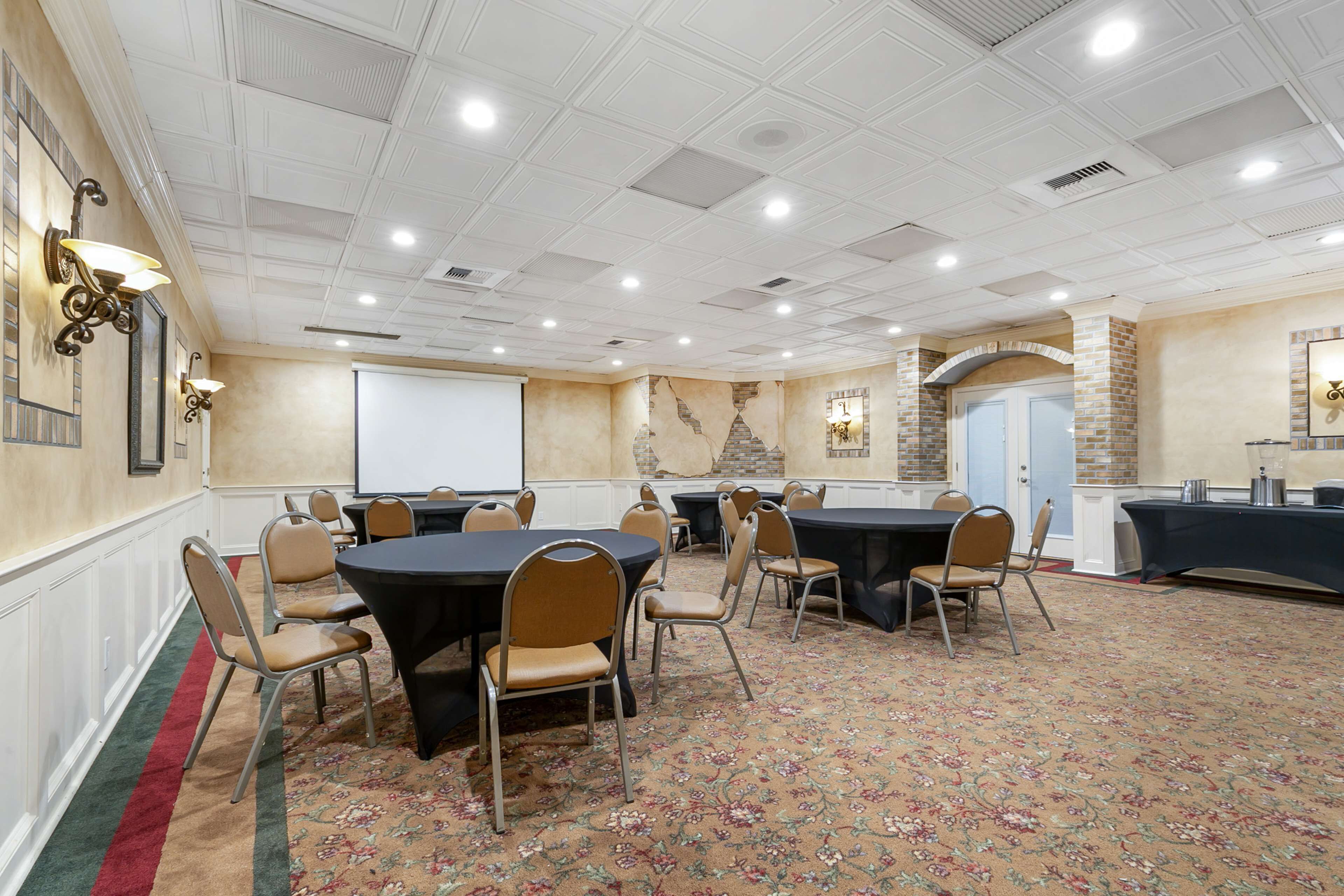 A conference room with round tables, chairs, a projector screen, and a carpeted floor.