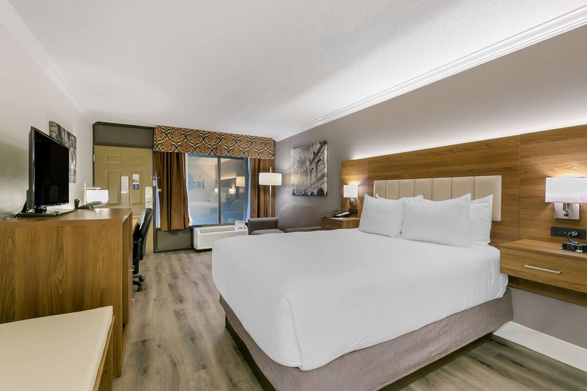 Habitación de hotel con una cama grande, un escritorio con televisor, un espejo y un cabecero de madera.