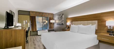 A hotel room with a large bed, a desk with a TV, a mirror, and a wooden headboard.