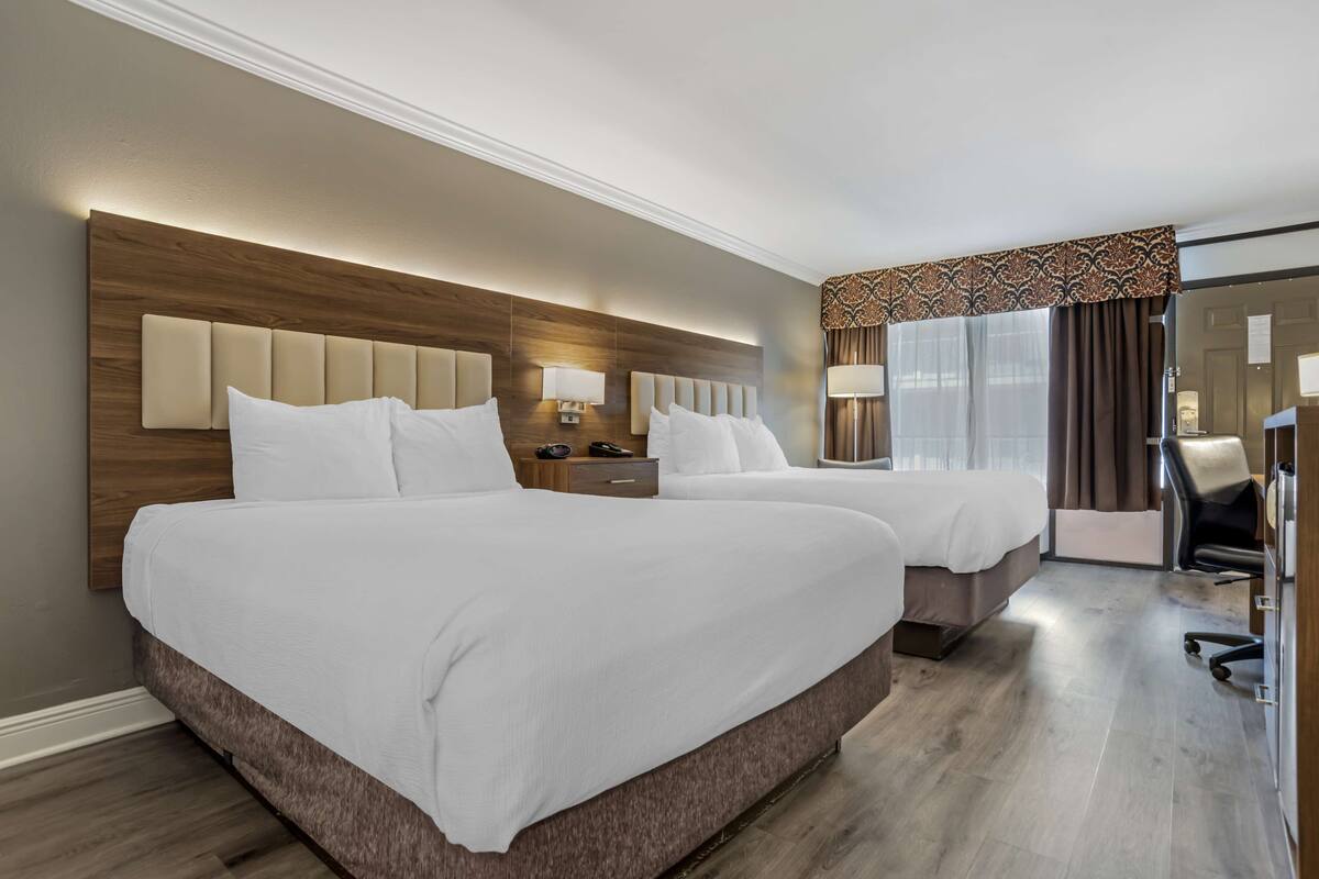 Habitación de hotel con dos camas, cabecero de madera, lámparas de noche, un escritorio y una silla.