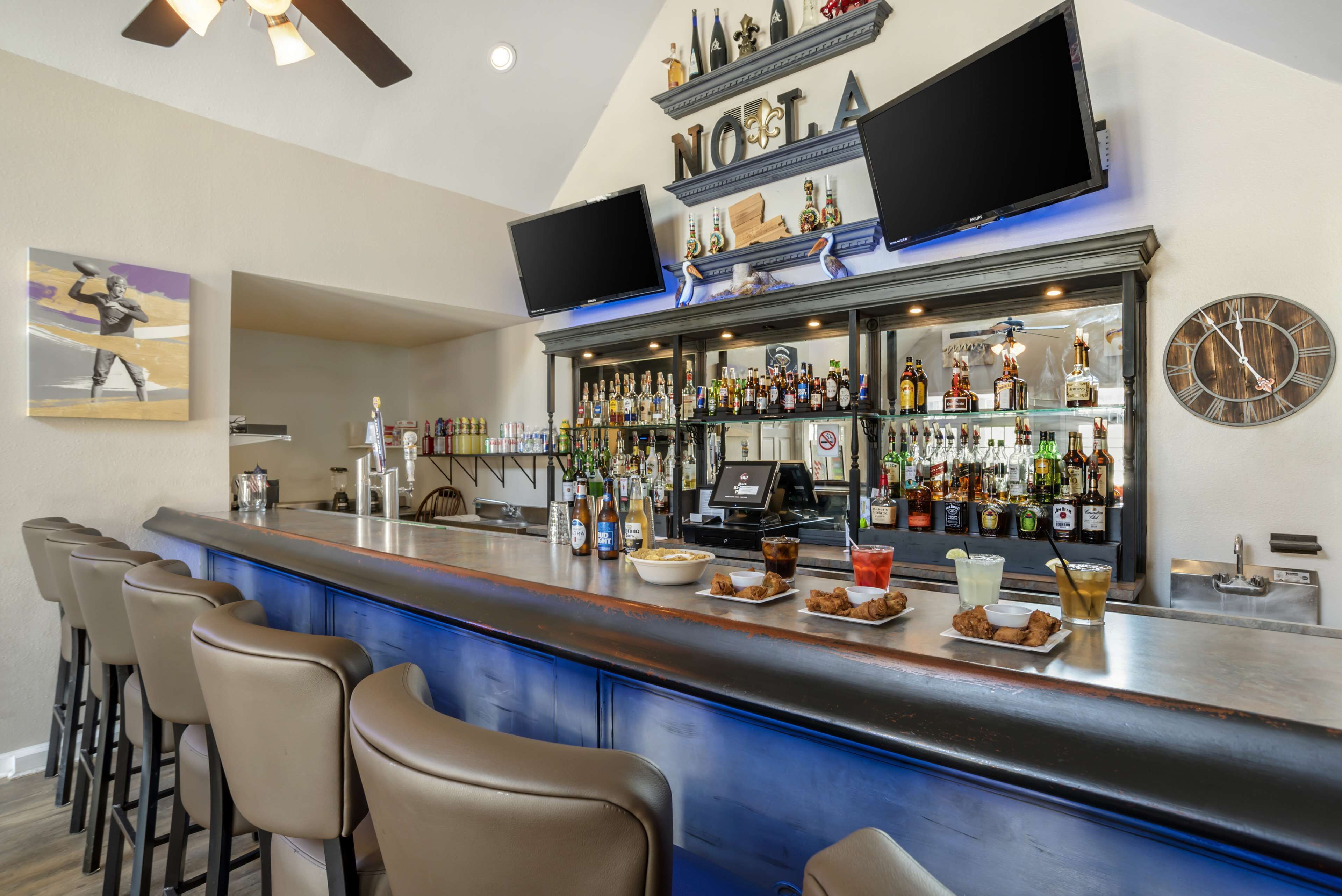 Zona de bar con mostrador, taburetes y una variedad de botellas y vasos.