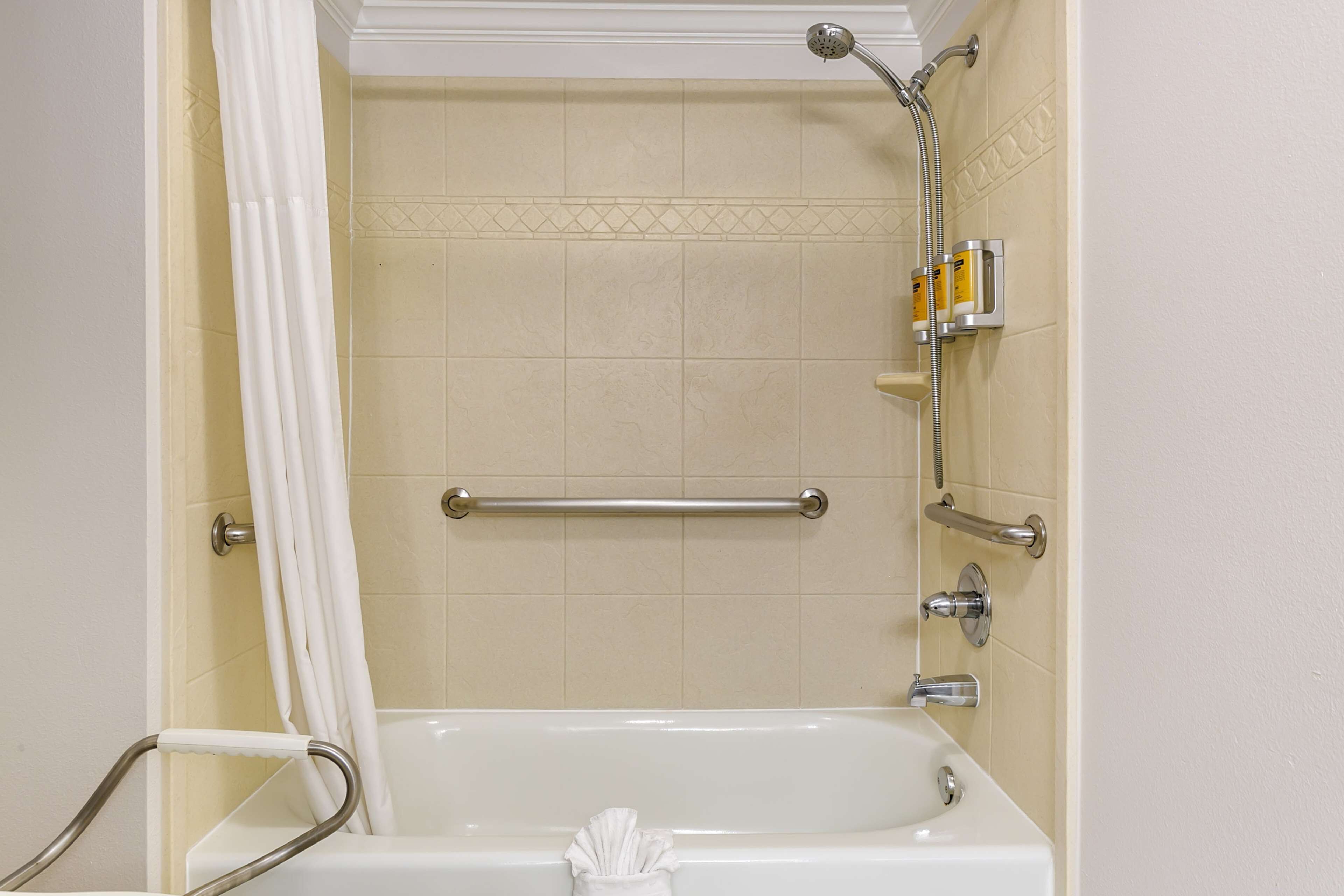 A bathroom with a bathtub, a shower, and a handrail.