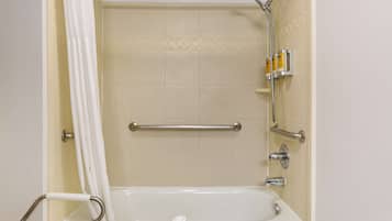 A bathroom with a bathtub, a shower, and a handrail.