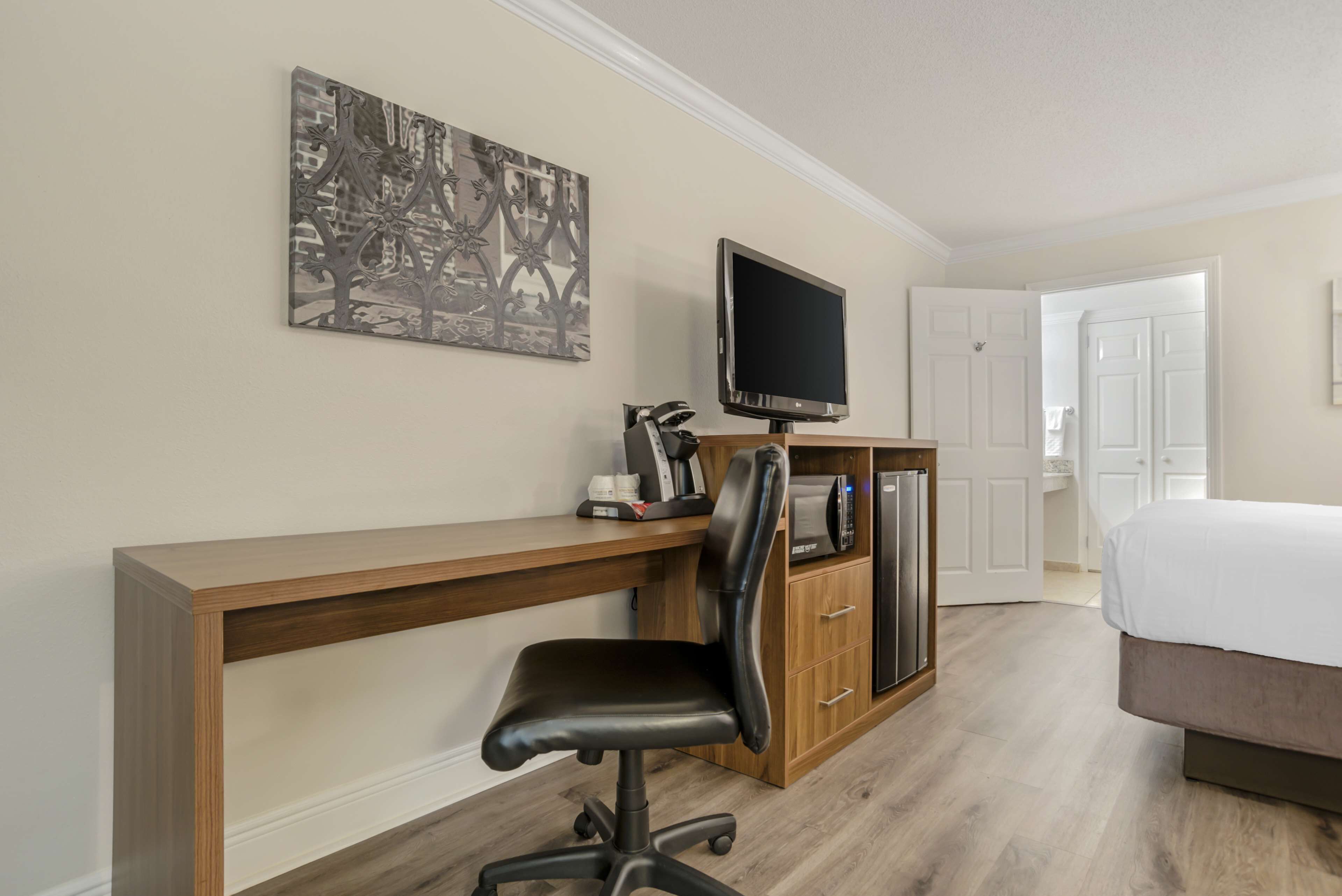 Habitación de hotel con escritorio de madera, una silla de oficina negra, televisor de pantalla plana, cafetera y un armario.