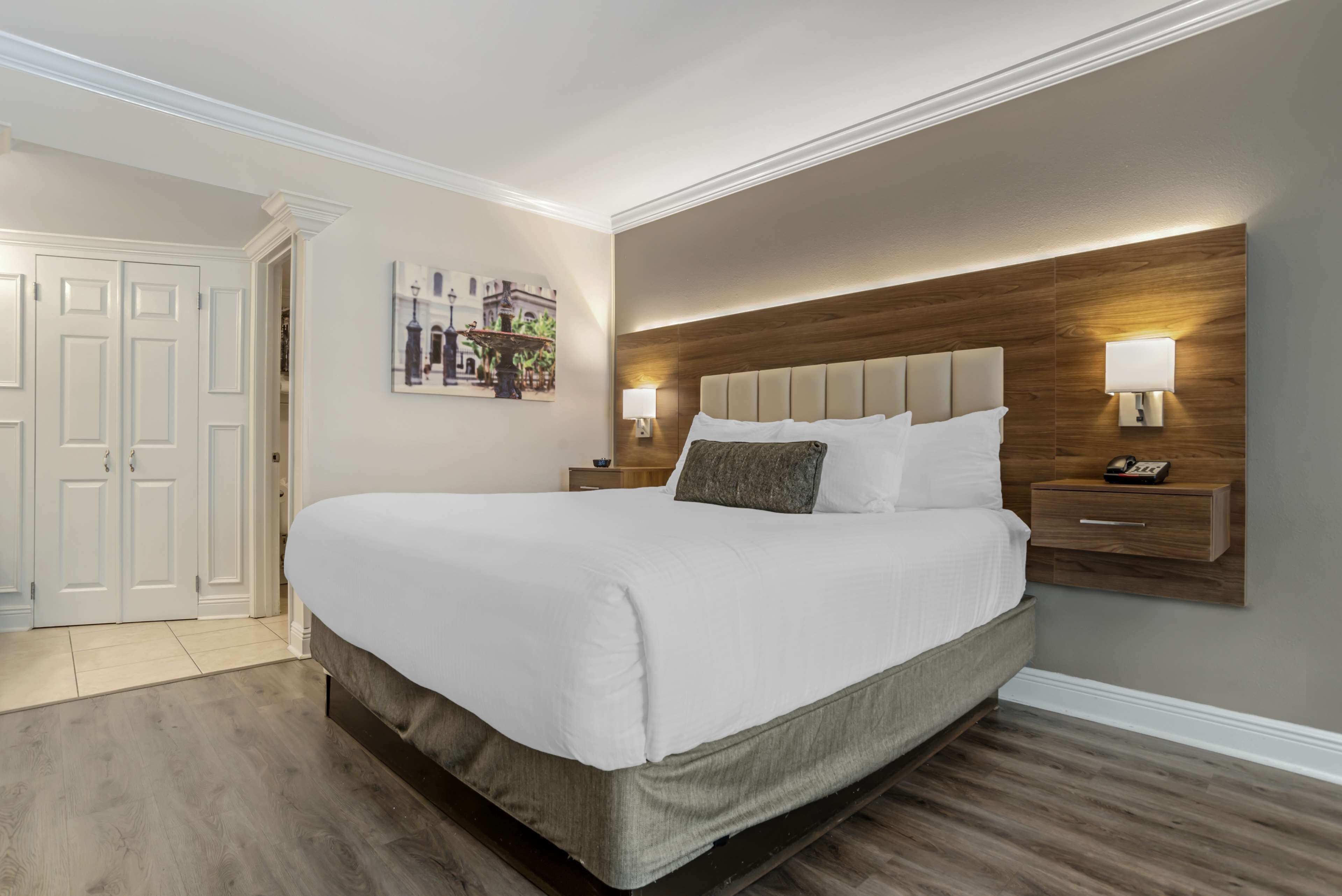 Une chambre à coucher bien aménagée, avec un grand lit, deux tables de chevet avec des lampes, une tête de lit en bois et une porte avec un panneau blanc.