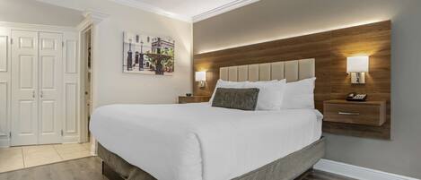 Une chambre à coucher bien aménagée, avec un grand lit, deux tables de chevet avec des lampes, une tête de lit en bois et une porte avec un panneau blanc.
