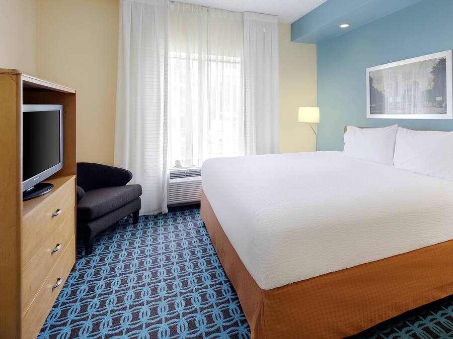 Habitación de hotel con una cama grande, televisión, escritorio y ventana con cortinas.