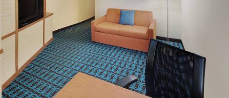 Habitación de hotel con sofá, televisión, escritorio y alfombra estampada.