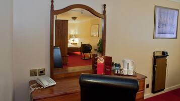 A hotel room with a wooden desk, a telephone, a coffee maker, a small cabinet, and a refrigerator.