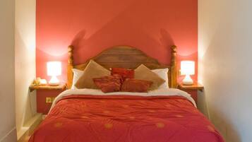 Una cama con cabecera de madera, dos lámparas de noche y una pared roja.